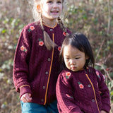 Children wearing the Little Green Radicals organic cotton snuggly knitted cardigan with a berry petal design. Dark purple cardigan with pink flowers details.