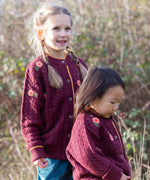 Children wearing the Little Green Radicals organic cotton snuggly knitted cardigan with a berry petal design. Dark purple cardigan with pink flowers details.
