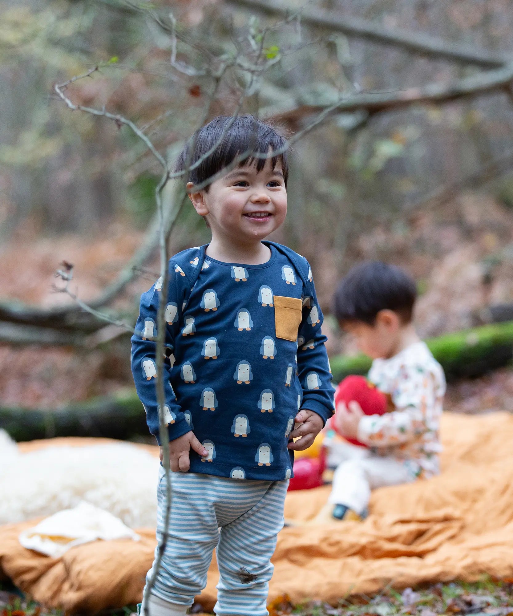 Child wearing the Little green Radicals blue penguin design playset outfit. Long sleeved organic cotton top in navy with penguins all over and light blue and white striped joggers.