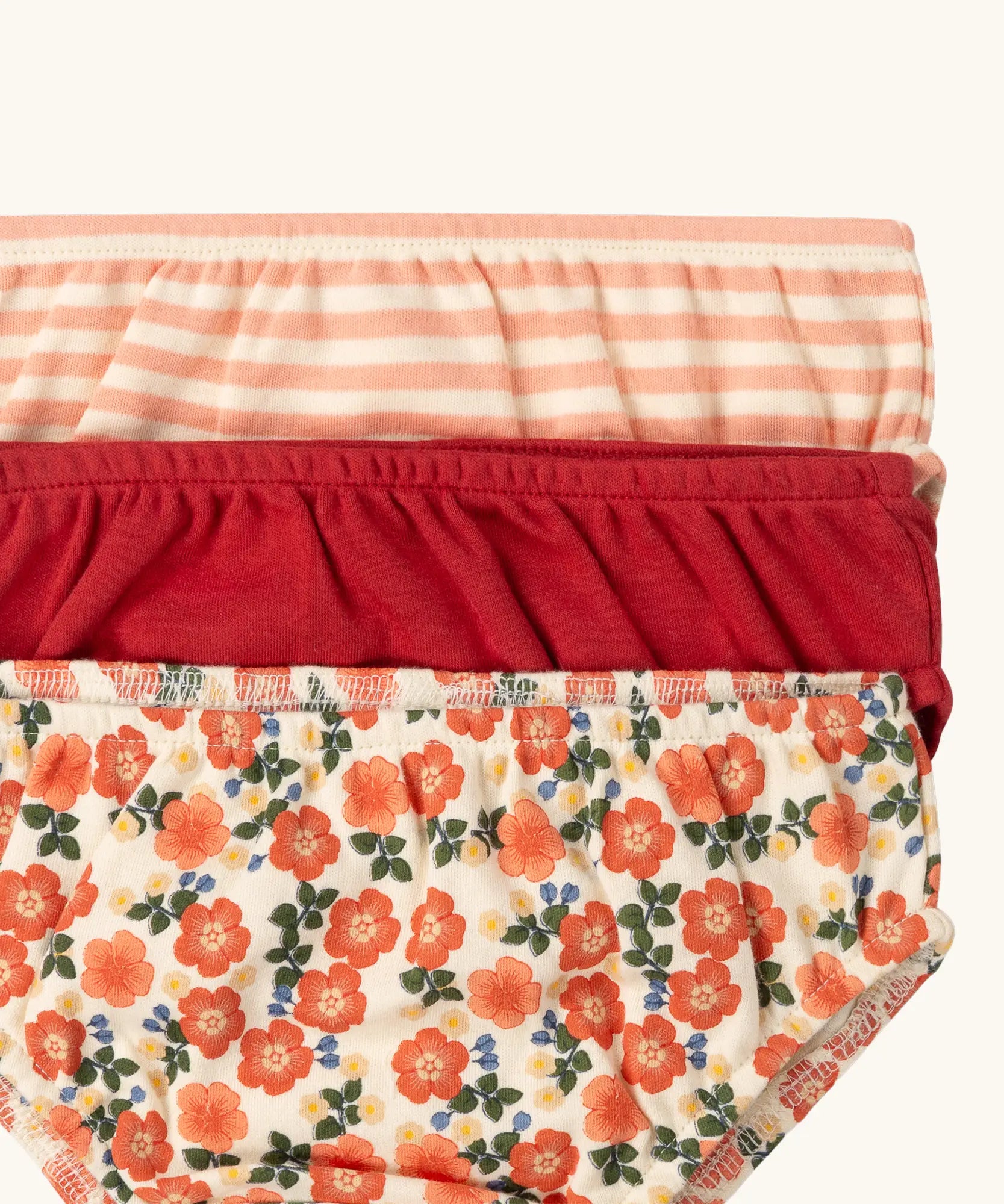 Close up of the elasticated waistbands on the Little Green Radicals organic cotton underwear in a 3 pack. Brief style pants one with a petals print, one red, one pink and white stripes. 