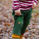 Child wearing the Little Green Radicals organic cotton woodland olive green knee patch joggers with yellow gold wellington boots.