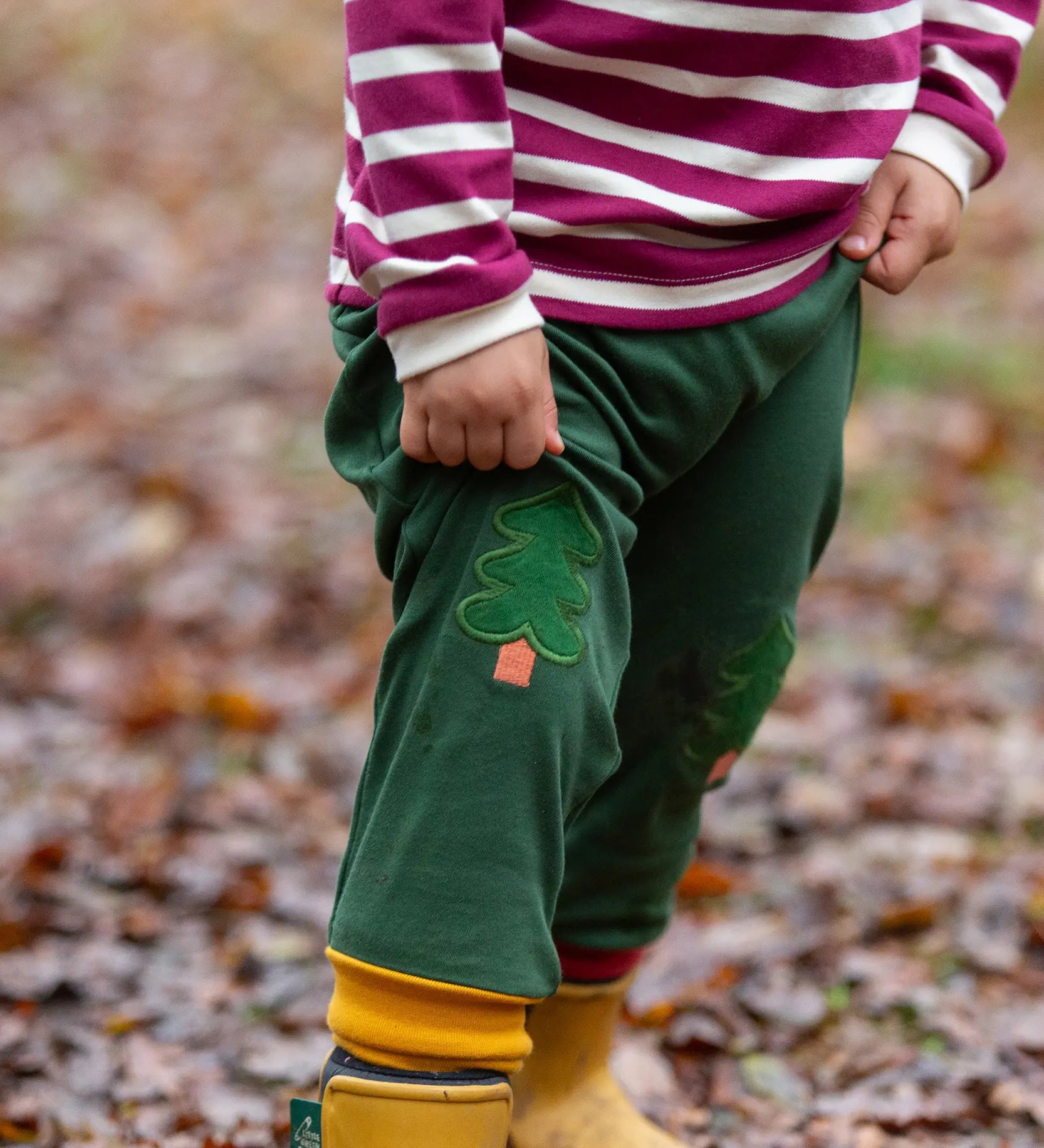 Child wearing the Little Green Radicals organic cotton woodland olive green knee patch joggers with yellow gold wellington boots.
