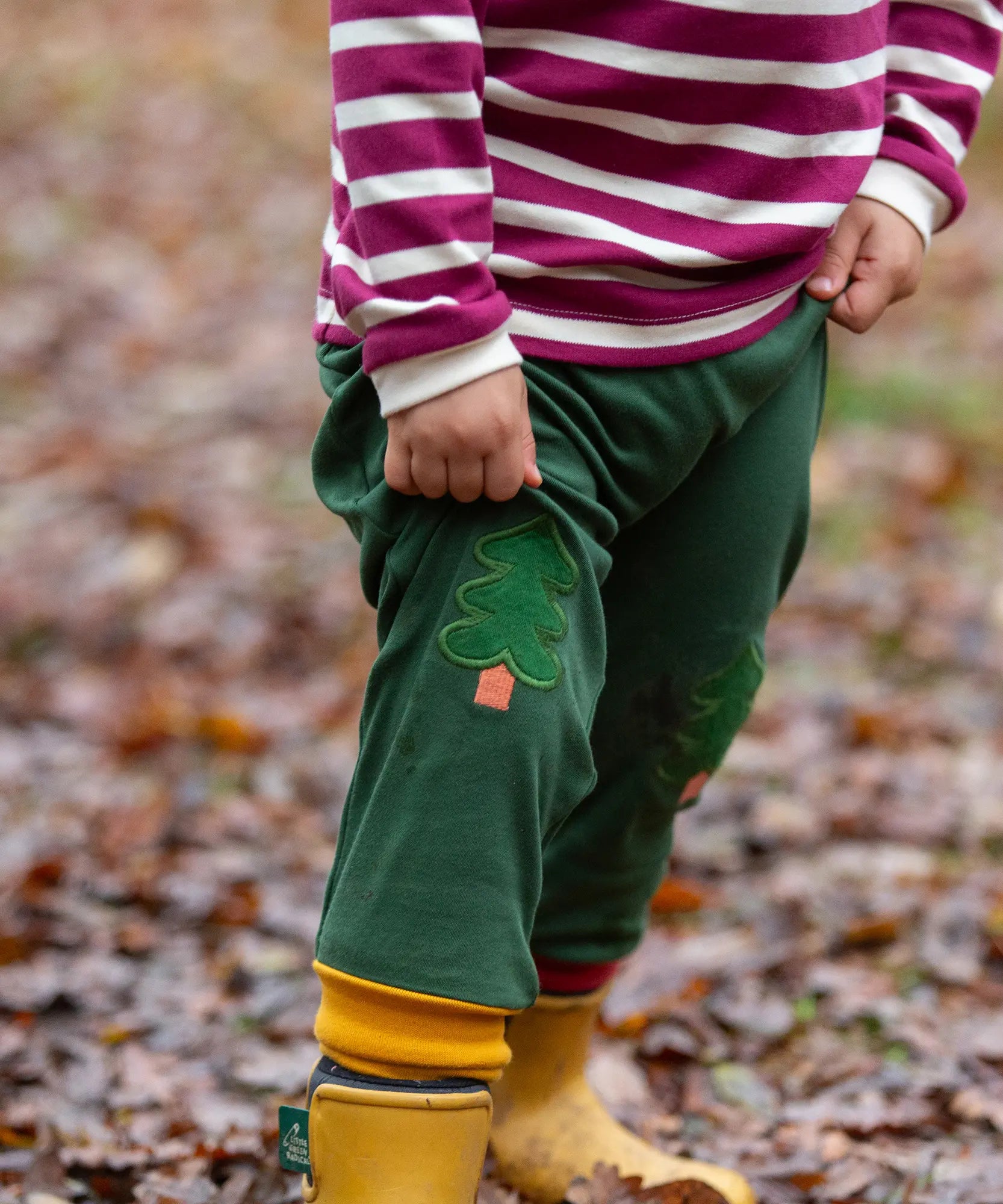 Child wearing the Little Green Radicals organic cotton woodland olive green knee patch joggers with yellow gold wellington boots.