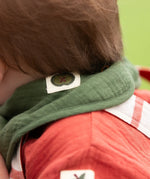 Close up of the green apple tag on the dark green bandana style bib from the Little Green Radicals blue moon organic cotton muslin bib set.