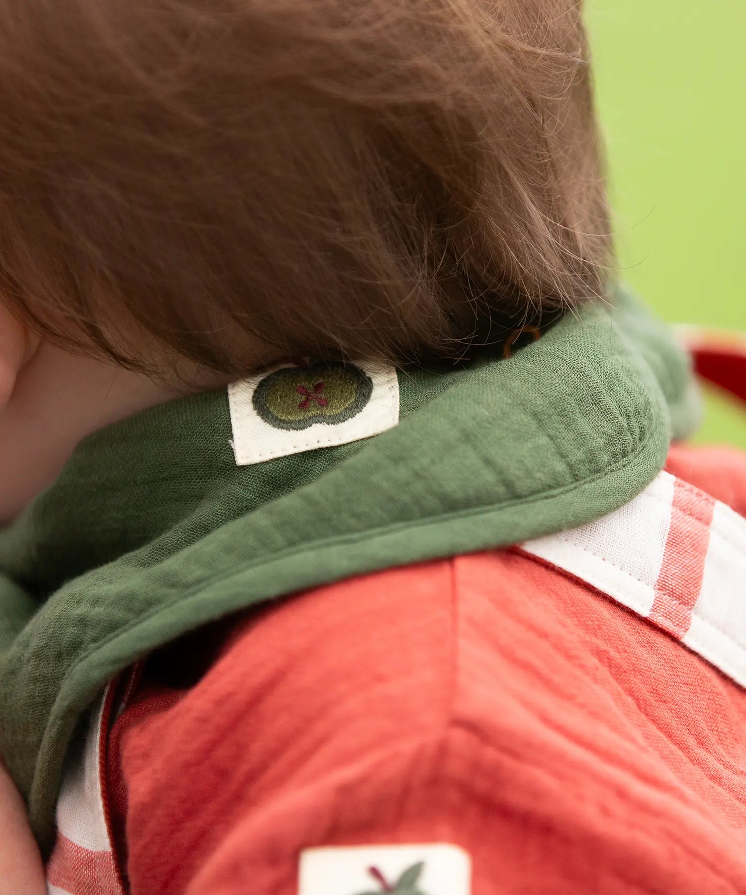 Close up of the green apple tag on the dark green bandana style bib from the Little Green Radicals blue moon organic cotton muslin bib set.