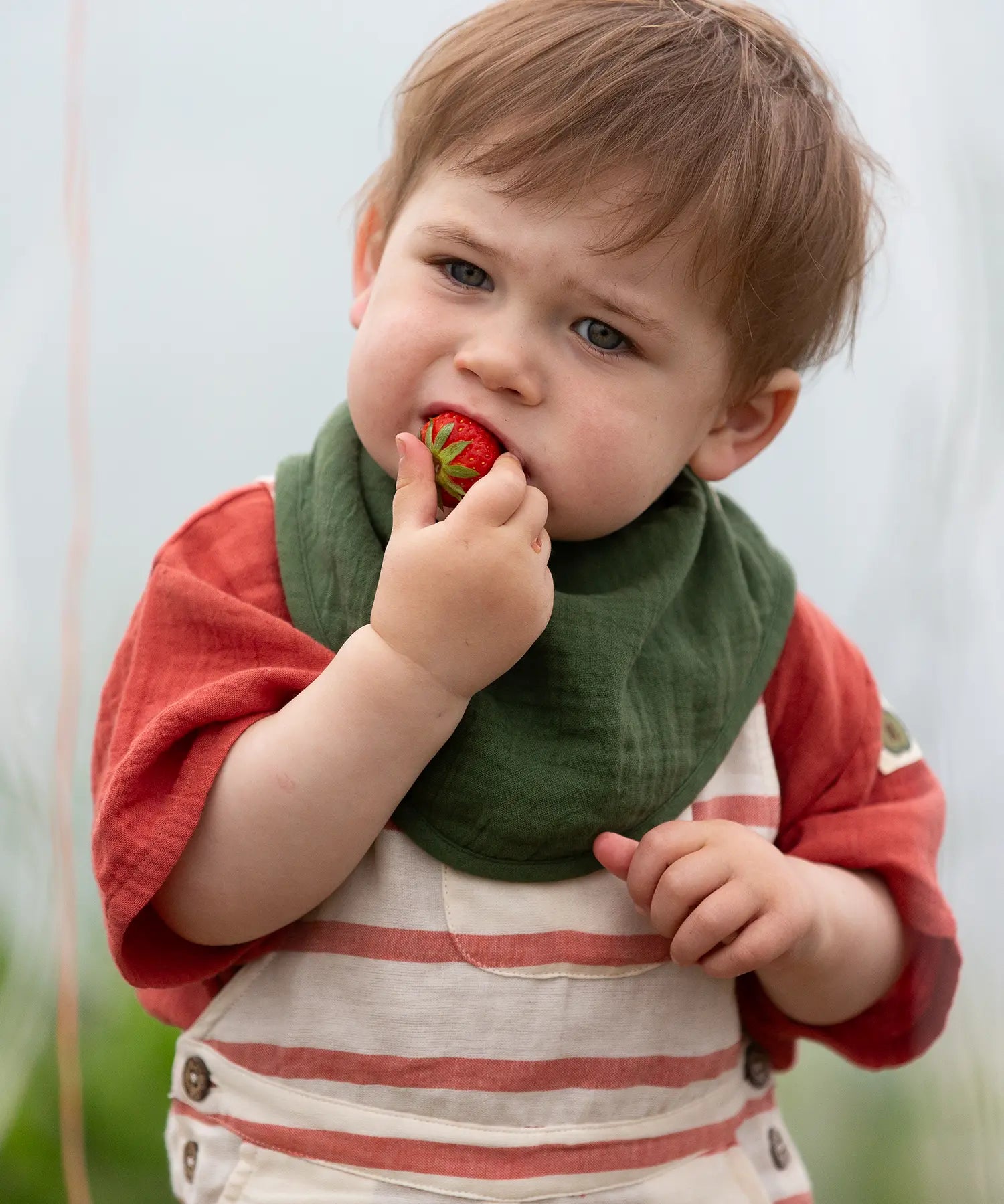 Child wearing the dark green bandana style bib from the Little Green Radicals blue moon organic cotton muslin bib set.