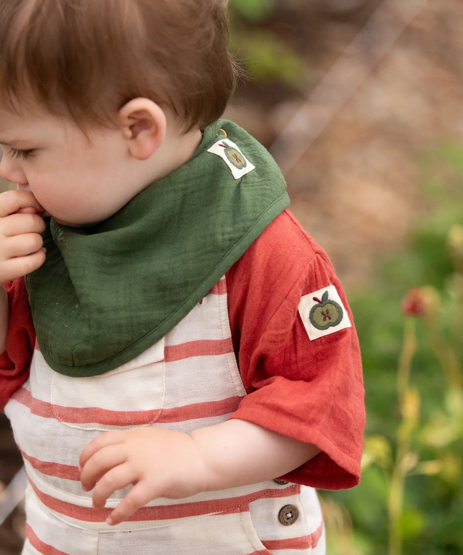 Child wearing the dark green bandana style bib from the Little Green Radicals blue moon organic cotton muslin bib set.