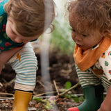 Child wearing the yellow ochre gold bandana style bib from the Little Green Radicals coral pink organic muslin bib set.