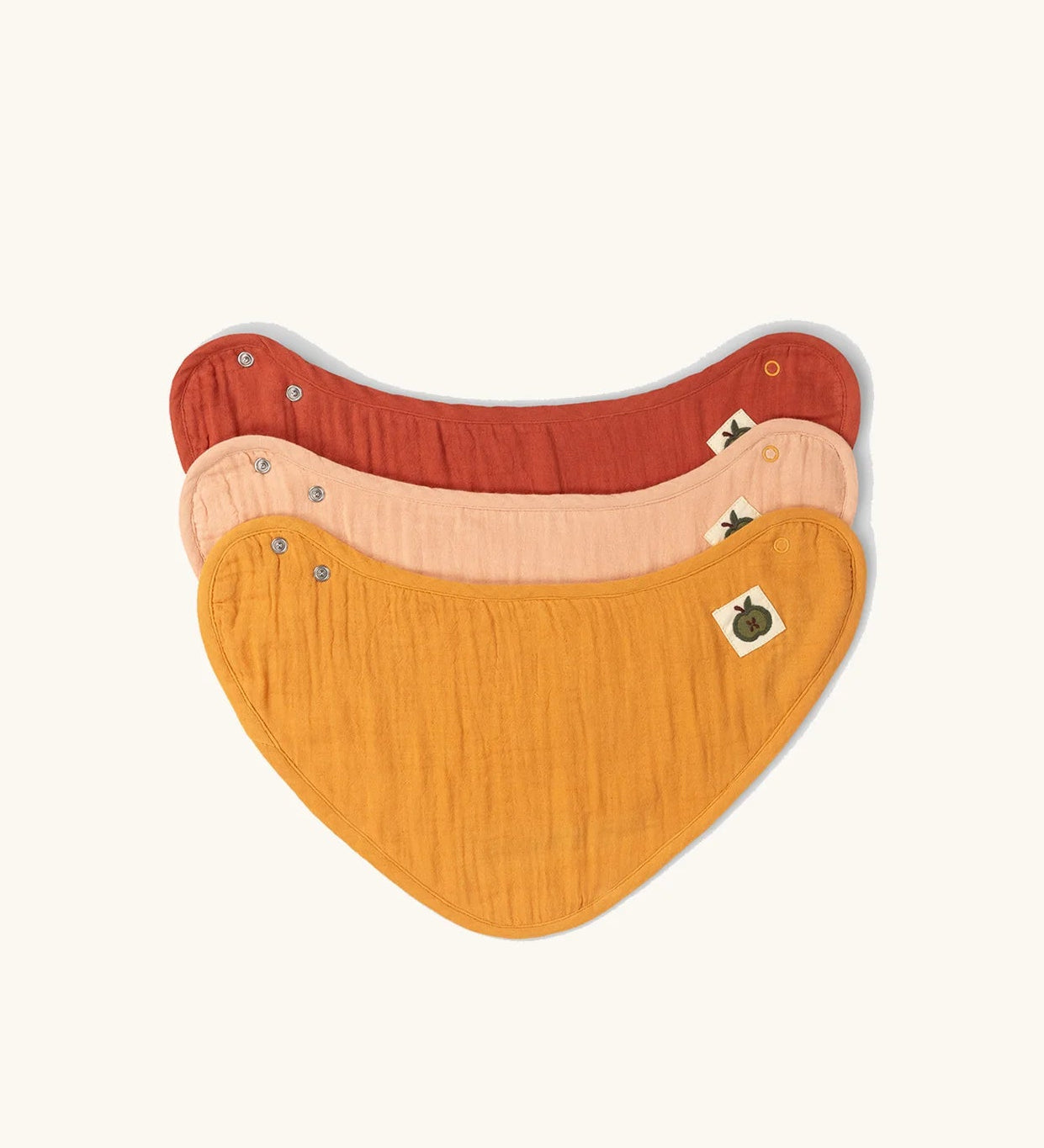 Little Green Radicals coral pink organic muslin bib set. Gold ochre yellow, red rust, and coral pink bandana style bibs in a pack of three.