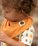 Close up of child wearing the ochre gold bib from the Little Green Radicals coral pink organic muslin bib set.