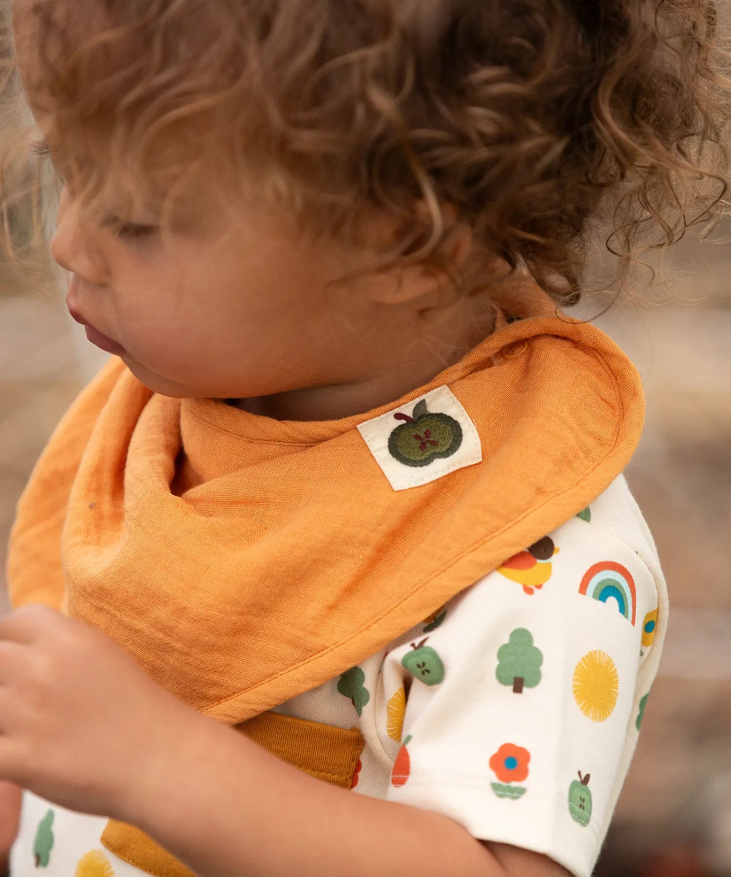 Close up of child wearing the ochre gold bib from the Little Green Radicals coral pink organic muslin bib set.