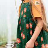Close up of the side pockets on the Little Green Radicals green orange blooms repeat print reversible pinny kids dress being worn.