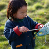 Child wearing the Little Green Radicals organic cotton snuggly knitted cardigan in midnight blue. Navy blue cardigan with red sleeve cuffs, green collar and yellow on the pockets.