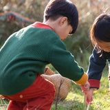 Child wearing the Little Green Radicals organic cotton snuggly knitted cardigan in olive green with orange corduroy trousers kneeling down. 