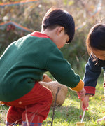 Child wearing the Little Green Radicals organic cotton snuggly knitted cardigan in olive green with orange corduroy trousers kneeling down. 