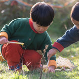 Child wearing the Little Green Radicals organic cotton snuggly knitted cardigan in olive green with orange corduroy trousers kneeling down. 