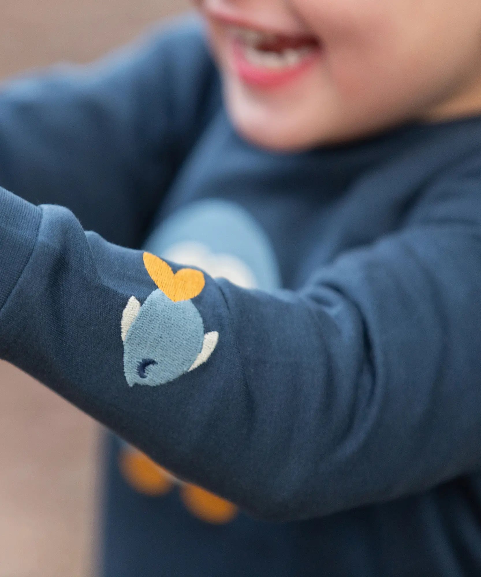 Close up of the fish embroidery detail on sleeve of the Little Green Radicals blue penguins applique long sleeve organic cotton top in navy.