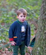 Child wearing the Little Green Radicals blue penguins applique long sleeve organic cotton top in navy with a midnight navy colour snuggly knitted cardigan and dark green joggers.