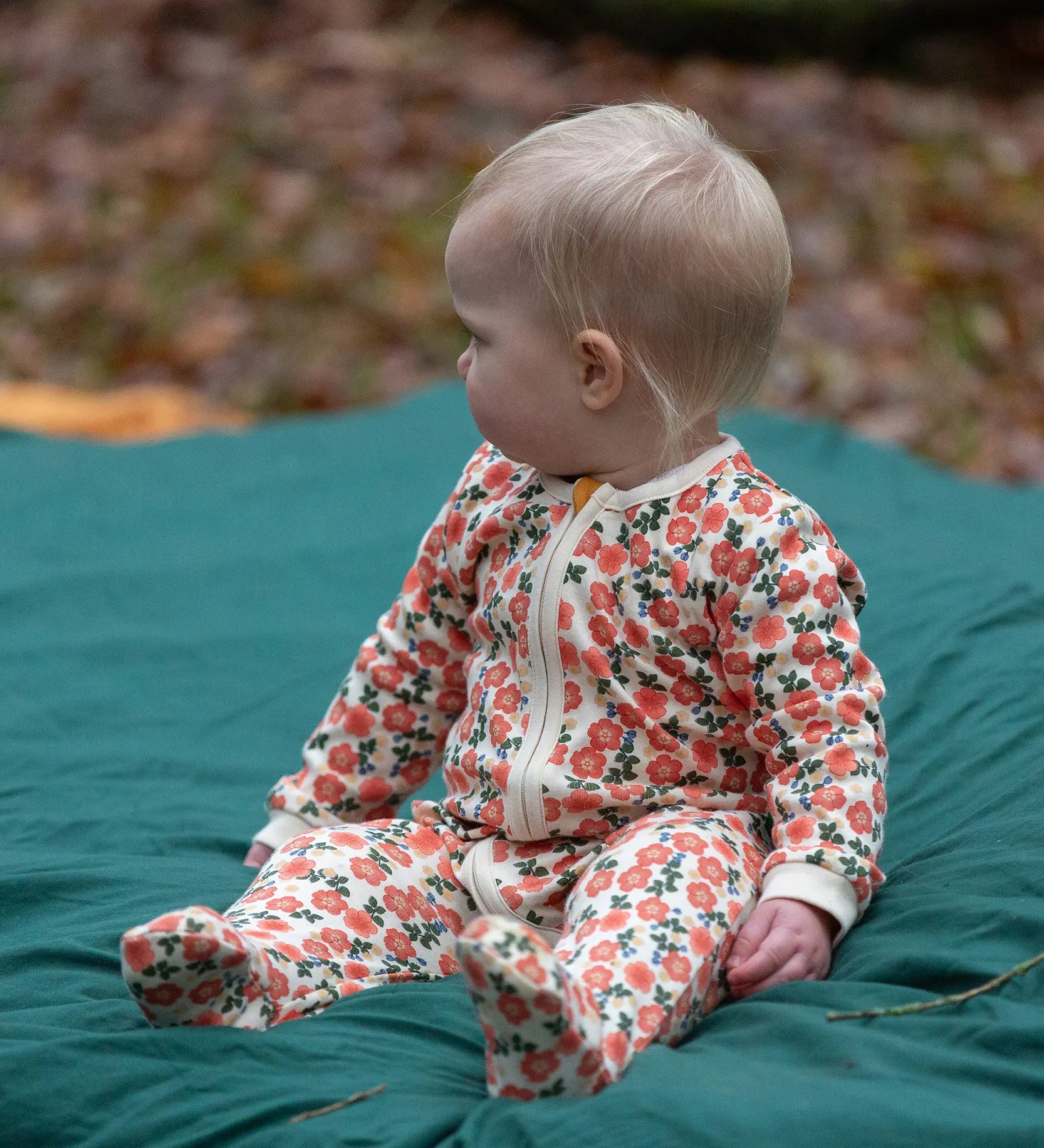 Baby wearing the Little Green Radicals petals GOTS organic cotton zip up babygrow. Natural coloured cotton with an all over pink flowers print.