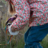 Close up of a child wearing Little Green Radicals pink petals recycled waterproof adventure Winter coat with blue corduroy trousers.