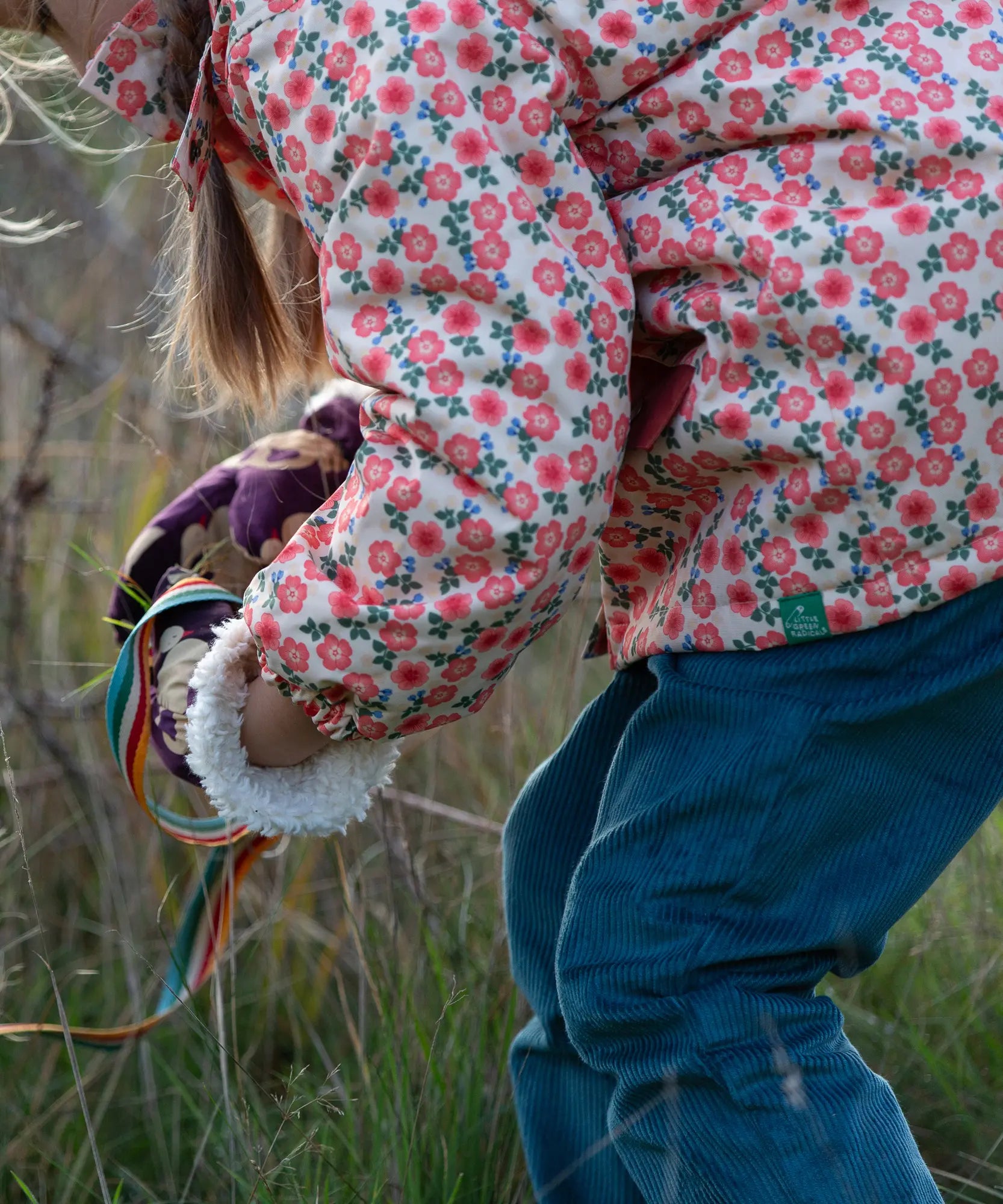Close up of a child wearing Little Green Radicals pink petals recycled waterproof adventure Winter coat with blue corduroy trousers.