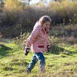 Child wearing Little Green Radicals pink petals recycled waterproof adventure Winter coat with blue corduroy trousers.
