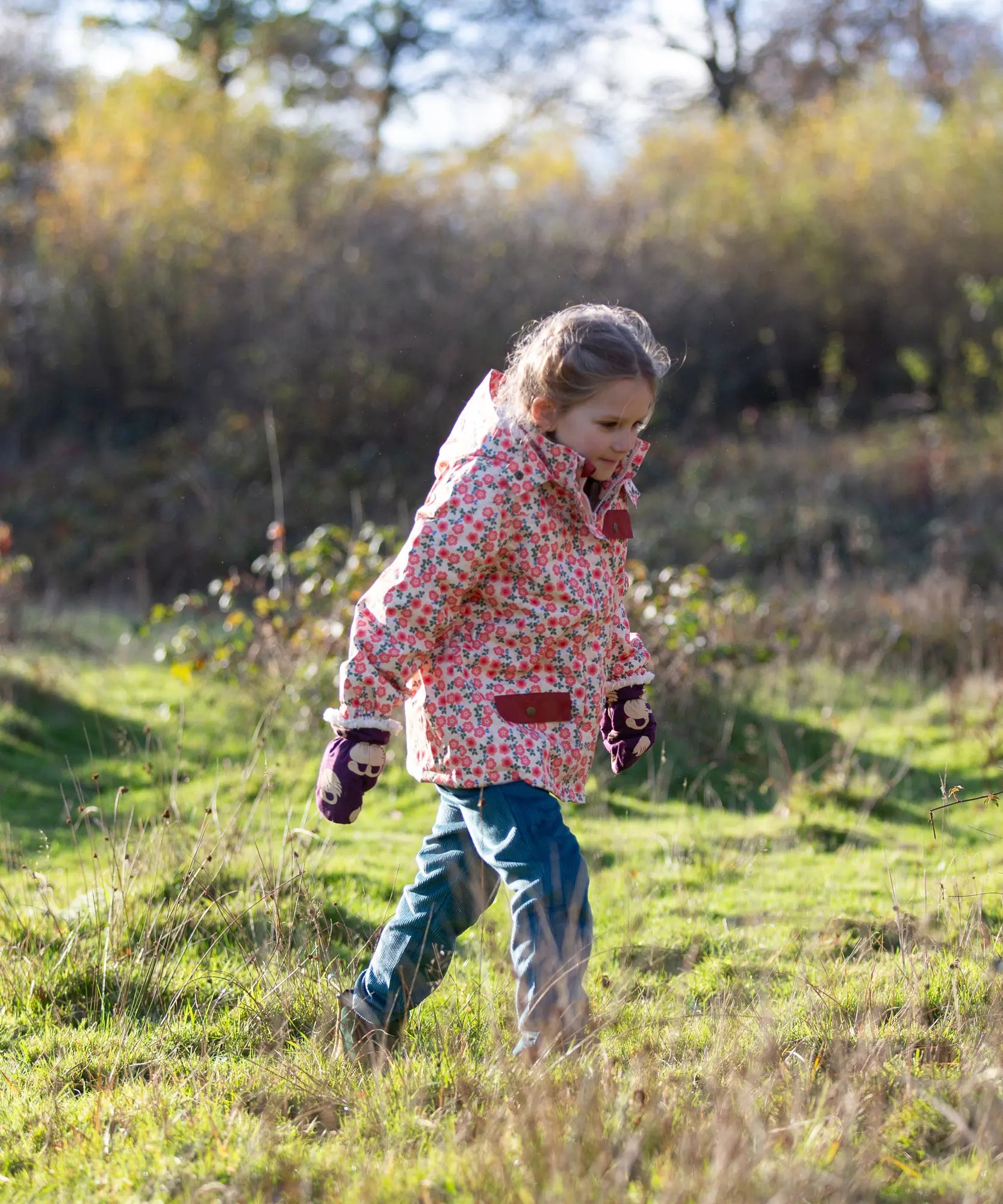 Child wearing Little Green Radicals pink petals recycled waterproof adventure Winter coat with blue corduroy trousers.
