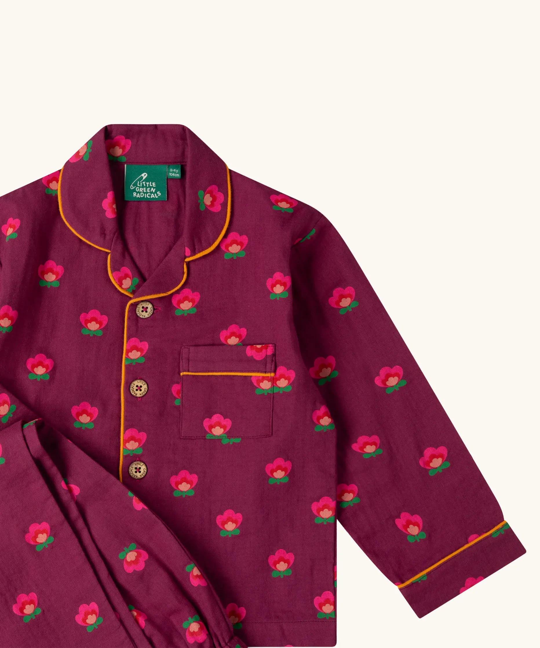 Close up of the Little Green Radicals pink flowers print organic cotton classic purple pyjamas. Long sleeve button up top with matching trousers.
