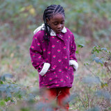 Child wearing a Little Green Radicals pink flowers purple organic cotton sherpa toasty coat with red trousers.
