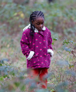 Child wearing a Little Green Radicals pink flowers purple organic cotton sherpa toasty coat with red trousers.