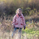 Child wearing Little Green Radicals pink petals recycled waterproof adventure Winter coat with blue corduroy trousers.
