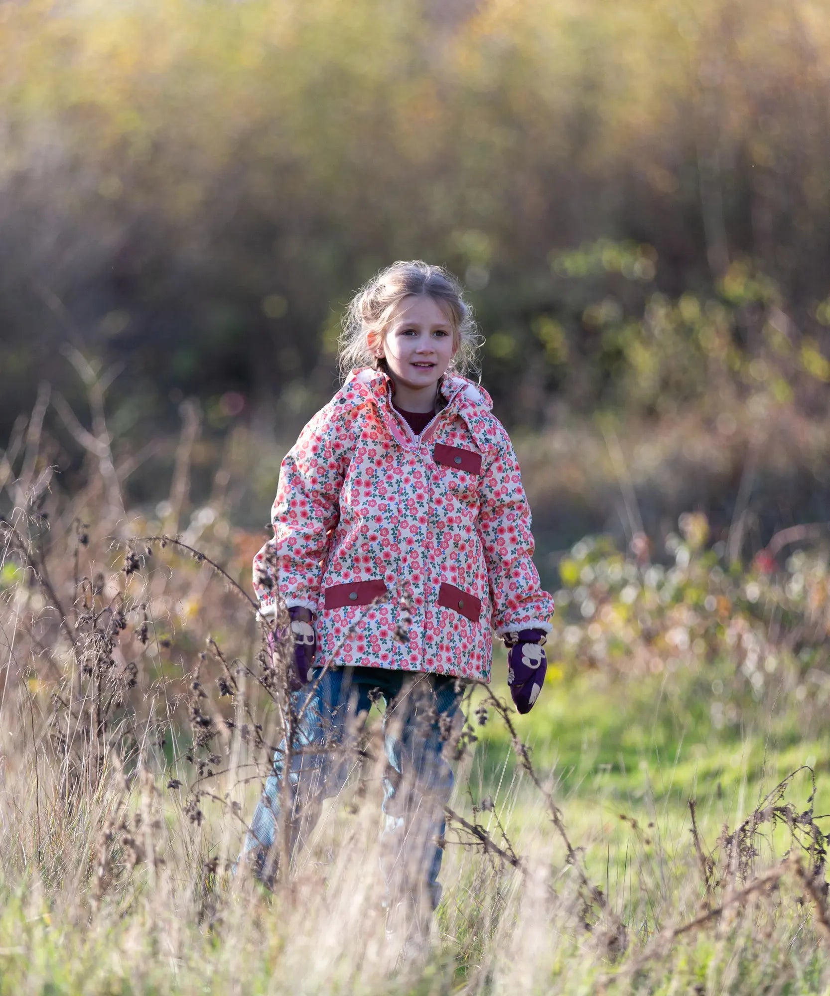 Child wearing Little Green Radicals pink petals recycled waterproof adventure Winter coat with blue corduroy trousers.
