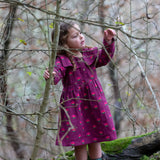 Child wearing the Little Green Radicals pink flowers sailor dress in purple with green wellington boots. 