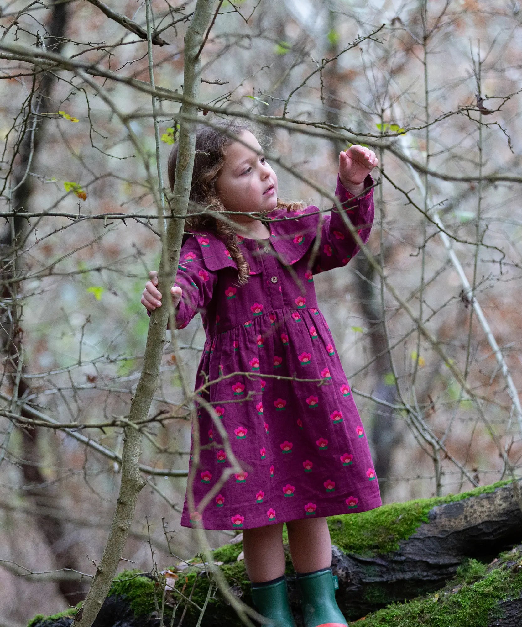 Child wearing the Little Green Radicals pink flowers sailor dress in purple with green wellington boots. 