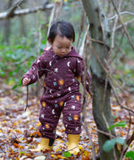 A child wearing the Little Green Radicals Organic Cotton Flying Birds Quilted Snug Suit. A maroon brown coloured suit with an all over print featuring flying birds, stars, moon and  sun. This snug suit is a part of a wide range of organic cotton clothing for children available here at Babipur. 