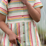 A close up of the button up front on the Little Green Radicals children's cream rainbow striped short sleeve dress being worn by a child.