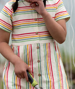 A close up of the button up front on the Little Green Radicals children's cream rainbow striped short sleeve dress being worn by a child.