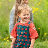 Child wearing the Little Green Radicals kids red apple print blue dungaree shorts with burnt ochre red muslin Henley t-short underneath.
