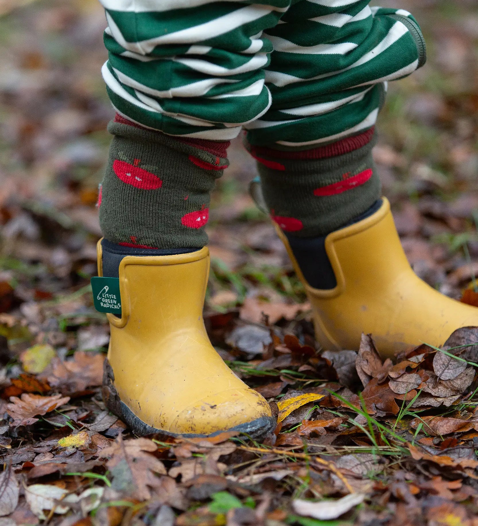 Child wearing the Little Green Radicals red apple terry boot socks with yellow gold wellington boots. 