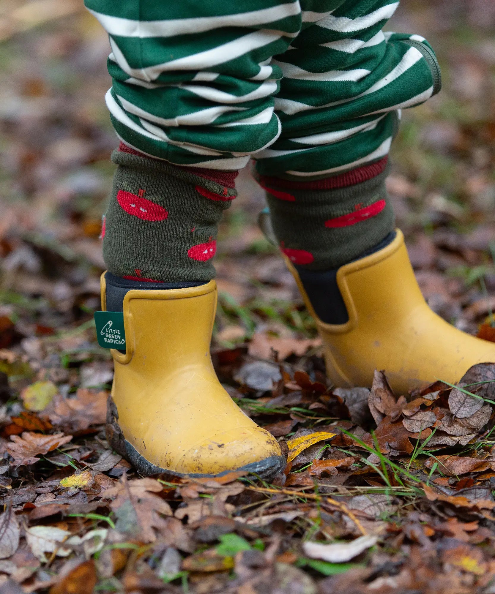 Child wearing the Little Green Radicals red apple terry boot socks with yellow gold wellington boots. 