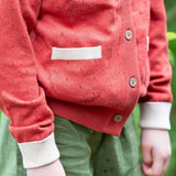 A close up of the pocket on the Little Green Radicals From One To Another Burnt Ochre Pointelle Knitted Cardigan with green coloured shorts. Little green Radicals have a wide range of organic cotton, Fairtrade children's clothing and outerwear available here at Babipur.