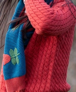 Close up of child wearing Little Green Radicals tulips knitted blue scarf. Blue scarf with red tulips.