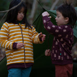 Two children standing in front of a green tent in the forest. Both are wearing the Little Green Radicals Reversible Easy Rider Jacket. One on the Brown Bears print side the other on a yellow gold and white stripe side. Little green Radicals have a wide range of organic cotton, Fairtrade children's clothing an outerwear available here at Babipur