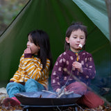 Two children sitting besides a campfire in the forest. Both are wearing the Little Green Radicals Reversible Easy Rider Jacket. One on the Brown Bears print side the other on a yellow gold and white stripe side. Little green Radicals have a wide range of organic cotton, Fairtrade children's clothing an outerwear available here at Babipur