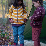 Two children standing in front of a tent in the forest. Both are wearing the Little Green Radicals Reversible Easy Rider Jacket. One on the Brown Bears print side the other on a yellow gold and white stripe side. Little green Radicals have a wide range of organic cotton, Fairtrade children's clothing an outerwear available here at Babipur.