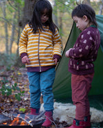 Two children standing in front of a tent in the forest. Both are wearing the Little Green Radicals Reversible Easy Rider Jacket. One on the Brown Bears print side the other on a yellow gold and white stripe side. Little green Radicals have a wide range of organic cotton, Fairtrade children's clothing an outerwear available here at Babipur.