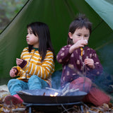 Two children sitting besides a campfire in the forest. Both are wearing the Little Green Radicals Reversible Easy Rider Jacket. One on the Brown Bears print side the other on a yellow gold and white stripe side. Little green Radicals have a wide range of organic cotton, Fairtrade children's clothing an outerwear available here at Babipur