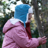 A child wearing the Little Green Radials sherpa fleece cosy hat in pale blue. This hat is a part of a wide range of organic cotton clothing and accessories for children available here at Babipur. 