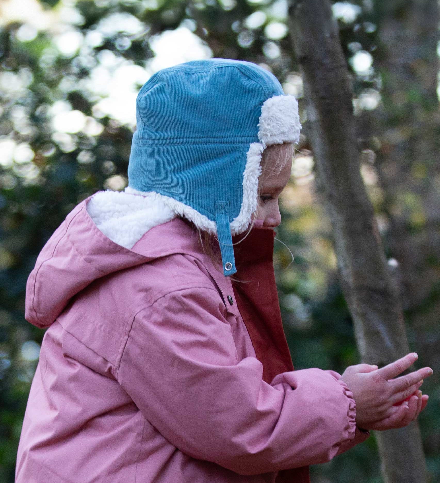 A child wearing the Little Green Radials sherpa fleece cosy hat in pale blue. This hat is a part of a wide range of organic cotton clothing and accessories for children available here at Babipur. 