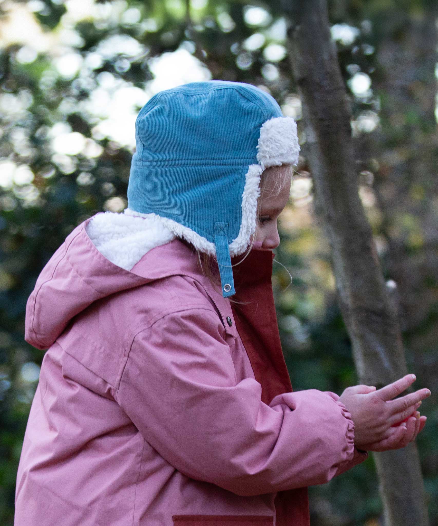 A child wearing the Little Green Radials sherpa fleece cosy hat in pale blue. This hat is a part of a wide range of organic cotton clothing and accessories for children available here at Babipur. 
